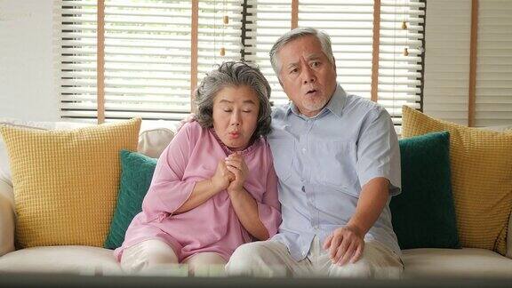 亚洲老夫妇在客厅里一起激动地看电视电影人们以放松、养老、退休、高级生活方式为家庭观念