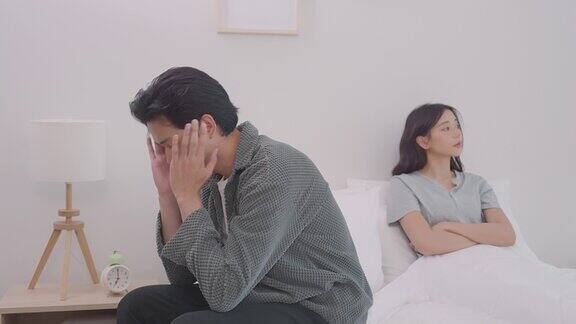 和妻子吵了一架后年轻悲伤的男人坐在床上关系的困难冲突与家庭观念不快乐的夫妻在床上有问题