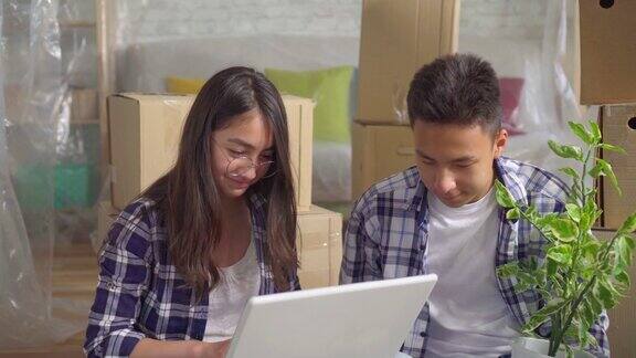 一对年轻的亚洲夫妇开车进入一个新公寓坐在地板上背景是盒子使用笔记本电脑的特写