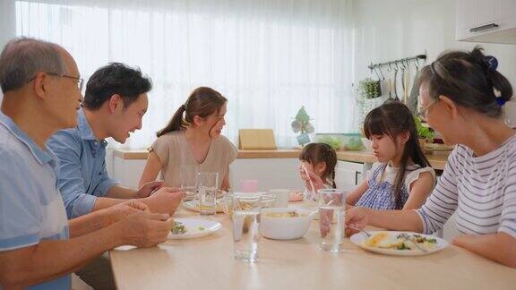 亚洲大家庭在家里的餐桌上共进午餐年长的祖父母年轻的夫妇和年幼的孩子女儿感到幸福享受在家里吃的食物活动关系