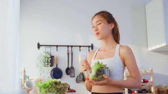 亚洲吸引人的运动女子拿着沙拉碗吃蔬菜美丽的运动女孩在运动服享受吃干净的蔬菜锻炼后的健康在家里饮食与健康食品理念