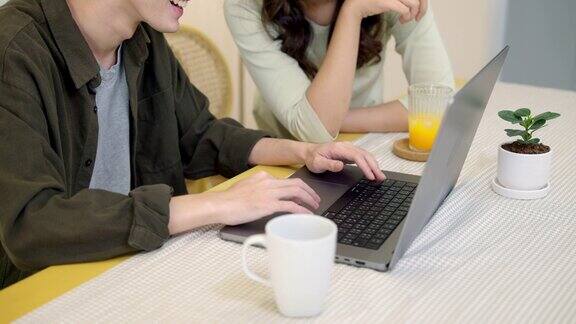 年轻夫妇坐在家里的桌子上一起使用笔记本电脑