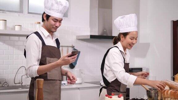 年轻的亚洲夫妇在厨房里愉快地做蛋糕和面包