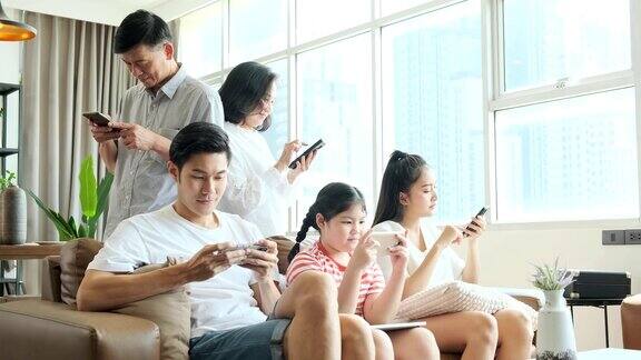 幸福年轻的亚洲大家庭在沙发上放松与可爱的小女儿和爷爷奶奶手一起使用智能手机应用程序在客厅家庭智能手机成瘾
