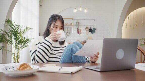 自由亚洲女士休闲服装使用笔记本电脑和喝咖啡在家里的厨房在家工作、远程工作、远程教育、保持社交距离、隔离预防冠状病毒