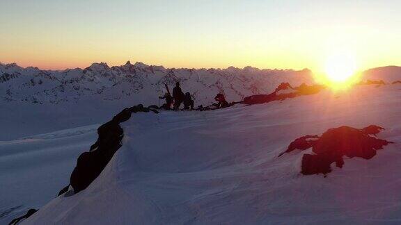 无人机拍摄的日落时分一群滑雪者站在一座雪山的边缘