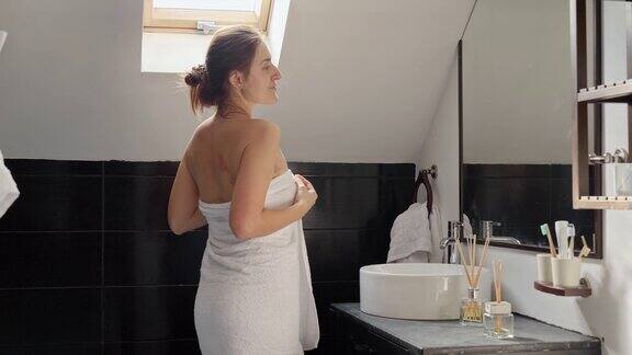 一个女人站在浴池里裹着毛巾对着镜子欣赏自己保持良好卫生和自我保健习惯