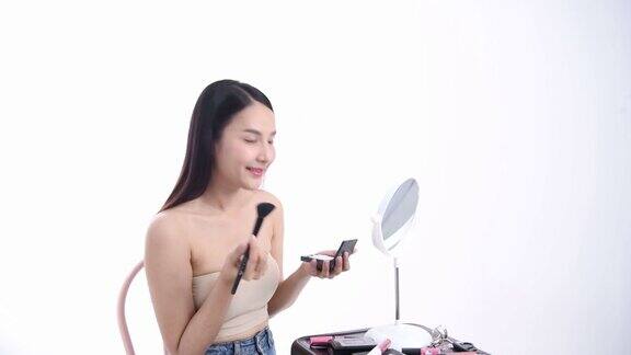 一位亚洲女性博主正在展示如何化妆和使用化妆品在摄像机前录制视频直播流媒体在工作室