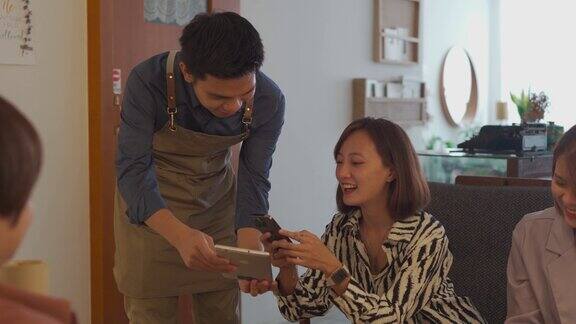 亚洲华人妇女使用手机应用支付账单在咖啡馆服务员与移动支付方式