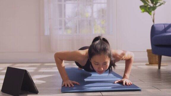 亚洲妇女穿着运动服做俯卧撑在运动垫上锻炼