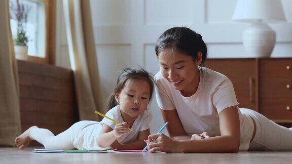 可爱的亚洲小女孩和妈妈在温暖的地板上画画