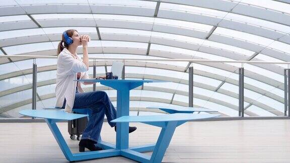 女商人在机场候机楼旅行时一边喝咖啡一边用笔记本电脑进行在线会议