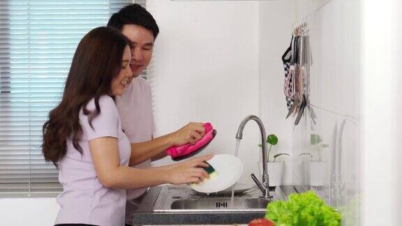 在家里的厨房里一对欢快的年轻夫妇一边跳舞一边洗碗