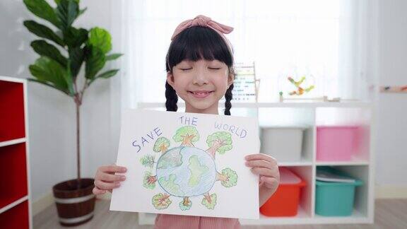 亚洲小学生女孩的快乐和微笑的脸她展示和持有她的绘画在拯救世界的主题她画的世界覆盖了许多绿色的树木