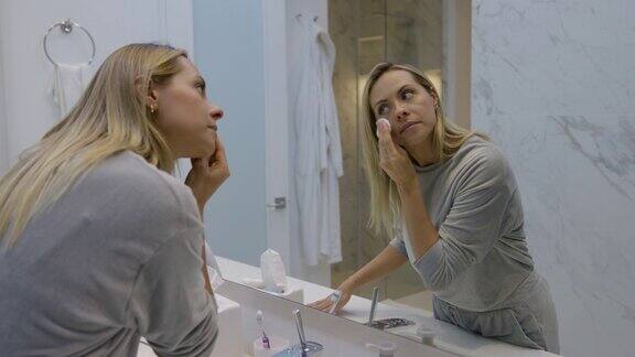 美丽的女人在浴室里用化妆棉洗脸