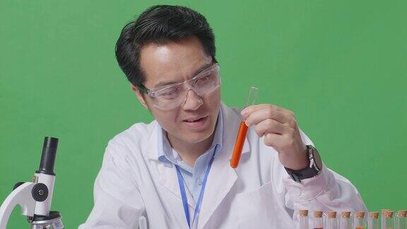 在绿屏背景的实验室里亚洲男科学家在用显微镜工作的桌子上用试管做实验并发出惊叹的特写