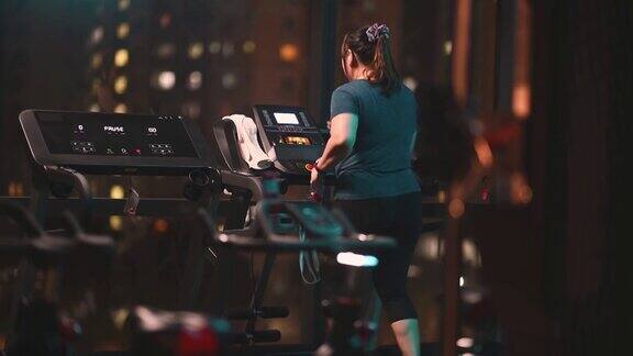 身体积极的亚洲华人女性晚上在健身房跑步机面对城市街灯心血管锻炼