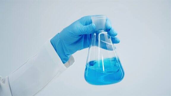 手在蓝色手套的玻璃烧瓶与蓝色液体