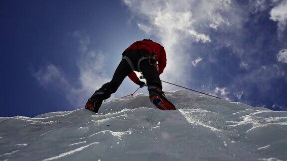 装备红色冰爪的登山运动员在晴朗的蓝天下攀爬冰墙