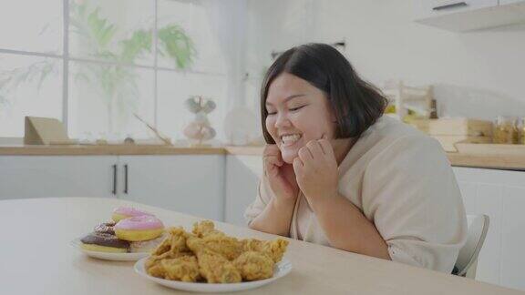 亚洲年轻的胖女人为盘子里的不健康食物感到高兴漂亮漂亮的胖女孩饿了准备在家里的餐桌上吃炸鸡和甜甜圈