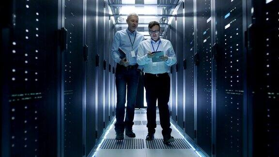 2名服务器技术员在数据中心工作一个使用平板电脑他们走过一排排的服务器机架