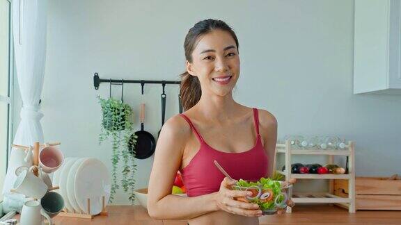 亚洲美女肖像拿着沙拉碗看着镜头漂亮的运动女孩穿着运动服在家里享受运动后吃干净的蔬菜的健康饮食和健康食品