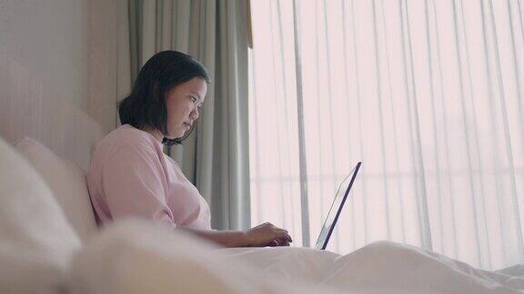 女人白天在卧室里用笔记本电脑工作