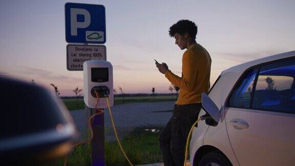 黄昏时分一名年轻的黑白混血男子在停车场给他的电动汽车充电