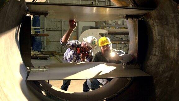 两名工人在工厂检查大型金属物体
