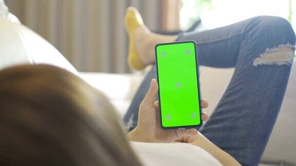 女人在沙发上用绿色屏幕的智能手机