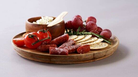 木板上放着脆饼、西红柿、葡萄和一碗奶酪