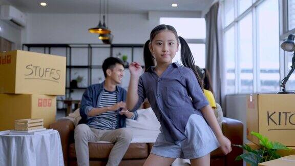 快乐亚洲女儿跳舞显示她的父母与欢快有趣的动作而休息后包装的东西和东西在纸箱搬家一个家庭在家里打包