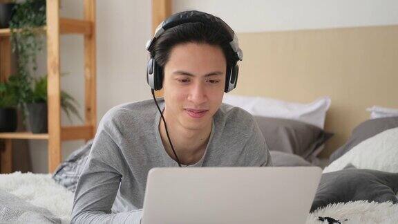 男人在床上用笔记本电脑听耳机音乐