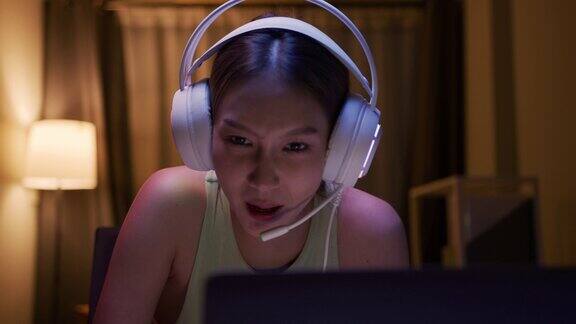 快乐的亚洲女人戴着耳机感到兴奋跳舞喊赢晚上玩电子游戏