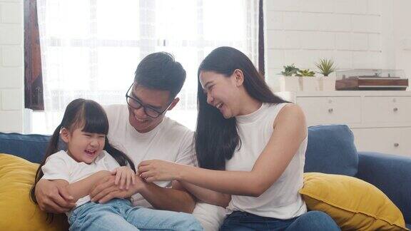 快乐快乐的亚洲家庭爸爸妈妈和女儿有乐趣拥抱在沙发上玩而生日在家里