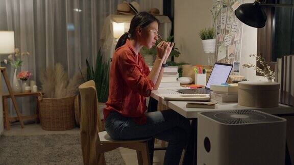 年轻的亚洲女性穿着休闲坐在桌子前拿着电脑笔记本电脑晚上在家里的客厅里对债务问题感到不开心对工作想法感到压力居家办公
