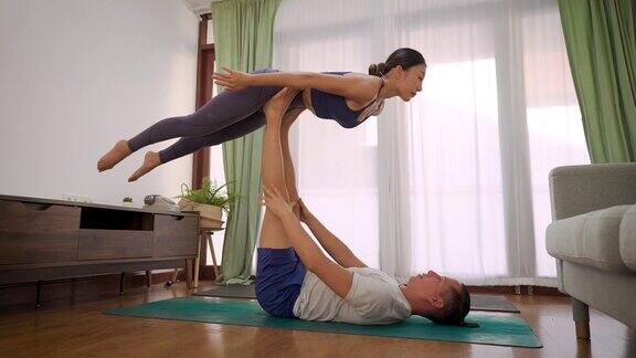 一个年轻的男人抱着女人的腿和胳膊在客厅里一起练习瑜伽夫妇在家健身