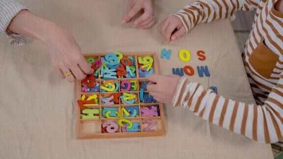 在家庭度假时母亲和儿子的手一起用各种颜色的木制字母组合成英语单词摆放在家里客厅的桌子上
