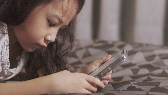 近距离观看正在玩智能手机、躺在床上的可爱的亚洲女孩的4K展示了年轻人享受、放松和享受数码设备的生活方式