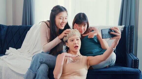 年轻的亚洲女性朋友们用智能手机自拍一起坐在家里的沙发上度过周末