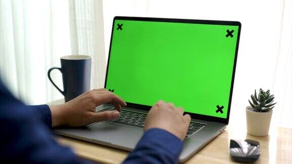 从肩膀上方拍摄的是一个年轻的商人正在用绿色屏幕的笔记本电脑工作