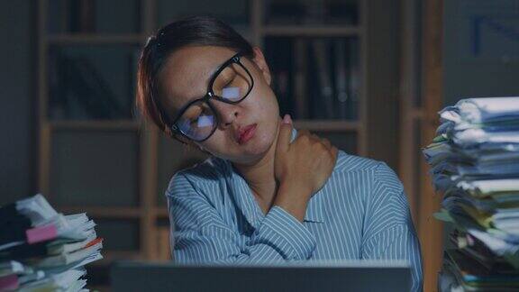 疲劳的亚洲办公室职员按摩颈部和肩部肌肉因为晚上在办公室加班使用笔记本电脑而感到疲劳