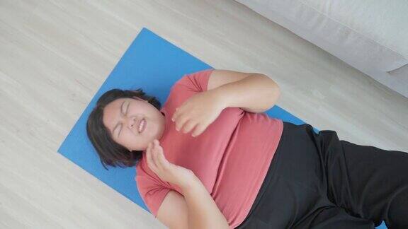 亚洲年轻的加码女孩试图坐起来锻炼在客厅有吸引力的特大号身材女孩为健康保健和使用垫子锻炼减肥遵循在线指导在家里