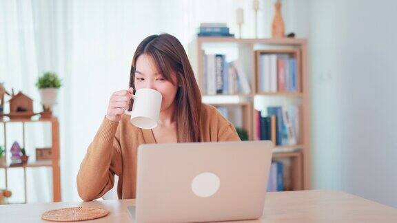年轻的亚洲妇女使用笔记本电脑和喝咖啡在家里工作场所女性工作笔记本在家里