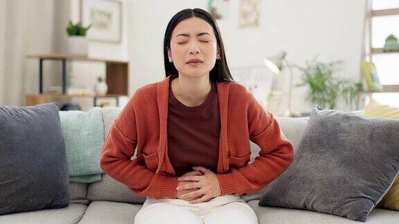 肠易激便秘和胃痛月经痉挛或食物中毒的生病妇女消化不良疼痛和亚洲女士腹泻腹胀和痛苦的经期痉挛在沙发上