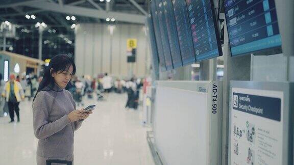 一名亚洲女子在机场用智能手机和手表查看登机牌时刻表