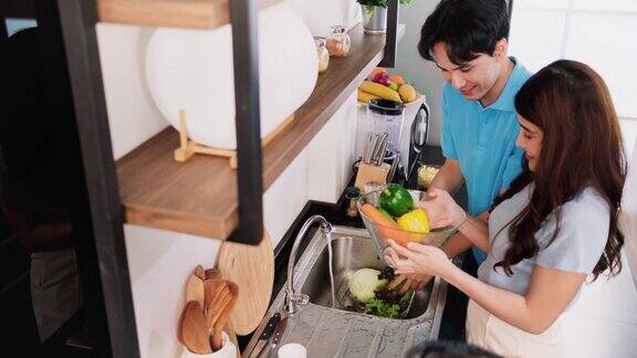 亚洲夫妇准备新鲜的有机蔬菜在家里厨房的水槽里清洗蔬菜做健康沙拉4k实时视频