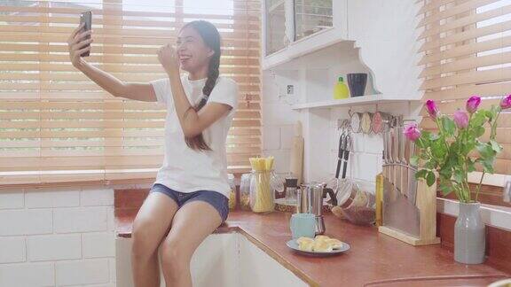 年轻的亚洲少女在家里做视频博客女性在厨房用智能手机制作视频到社交媒体生活方式女人在家里放松上午