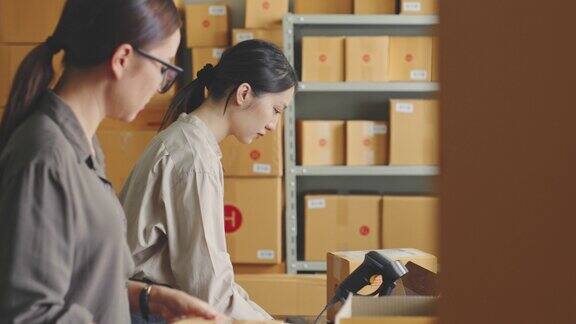 亚洲妇女在网上商店仓库工作包装产品到包裹纸箱网上电子商务零售的小商业概念