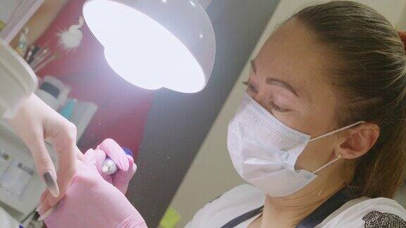 肖像女美甲师正在给客户锯指甲护理美容指甲美容院美甲服务硬件修指甲去除材料在美容院掌握在手套上钉指甲的程序